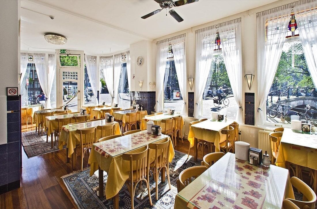 Breakfast room laid with yellow linen, bentwood chairs and stained-glass windows onto the canal
