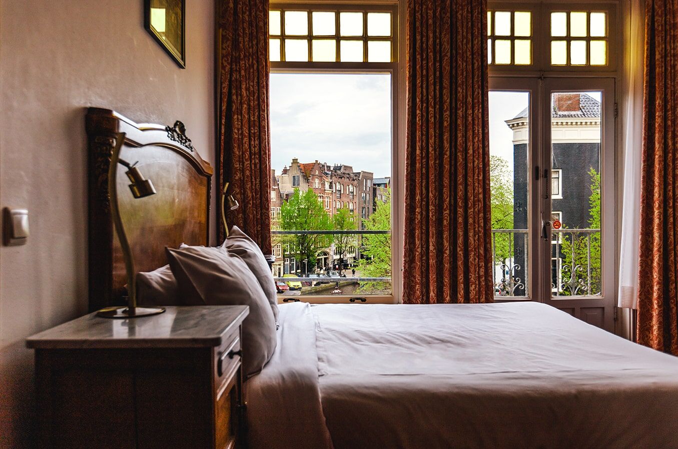 Bed beside tall canal-facing windows, with a carved wooden headboard and a brass reading lamp